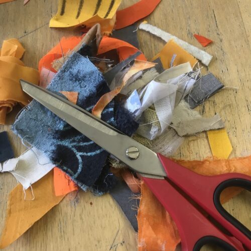 Small pieces of different shaped fabric in orange, blue, white, mustard colours with a large pair of scissors