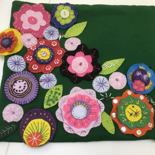 Dark green cushion cover with multi-coloured felt flowers and leaves covering most of the cushion