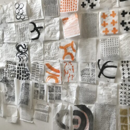 Lots of small squares of fabric in white with black or orange abstract or geometric patterns