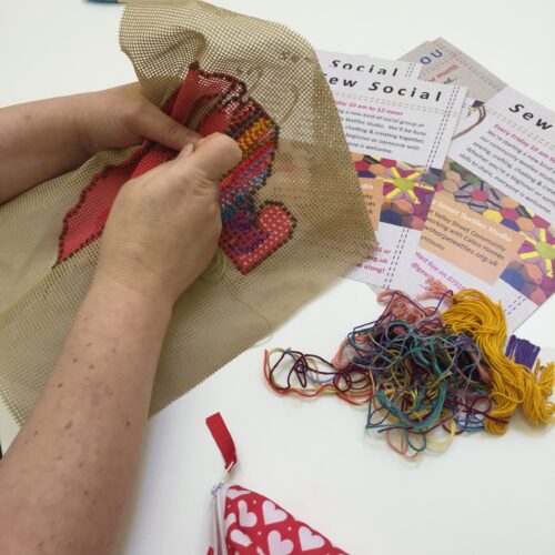 Hands sewing with pattern information and threads positioned on a table