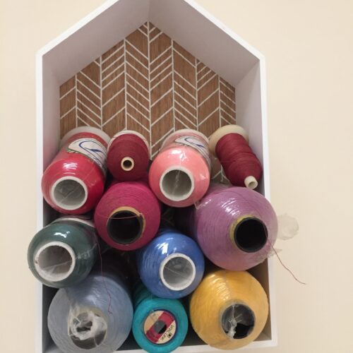 Overhead view of a box of different coloured threads on bobbins of different sizes