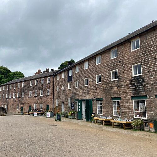 Row of three-storey reddy brown mill buildings with dark green painted doors and a courtyard.