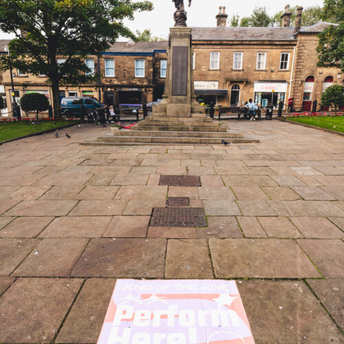 Stone paving leading to a statue on a plinth in the middle of a square with two storey brick buildings at one end