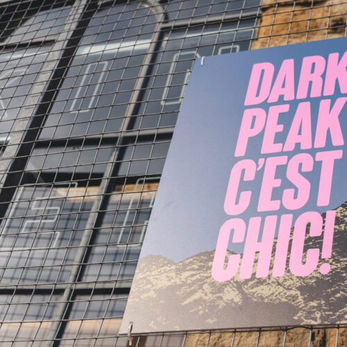 Poster on an outside stone wall next to a large window. Poster reads: Dark Peak C'est Chic!