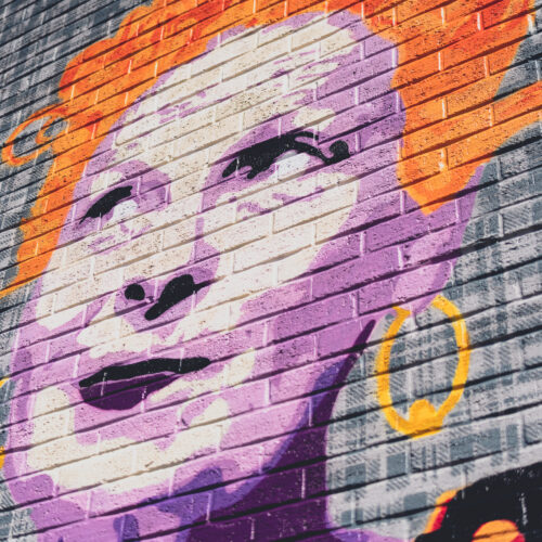 Wall mural of fashion designer Vivienne Westwood with her skin painted in pink and white, with a shock of orange hair and yellow hoop earrings